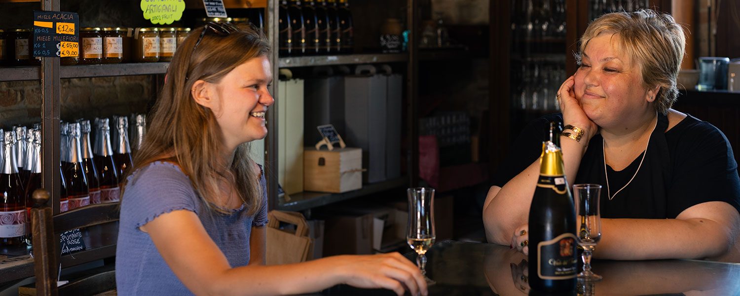 Reisende und Gastgeberin beim Prosecco-Trinken im Hofladen eines Weinguts